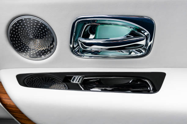 Door handle with power window control buttons of a luxury passenger car. White perforated leather interior with stitching and wood panel. Modern car interior details.. Car inside