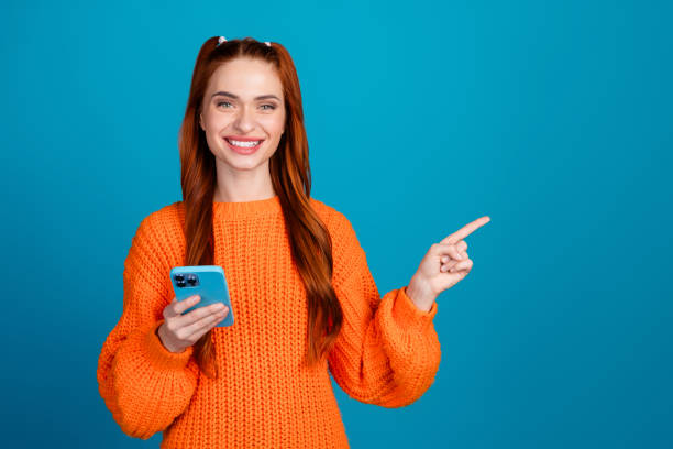 istock Photo of cheerful pretty lady dressed orange pullover writing sms modern gadget pointing empty space isolated blue color background 2181703802