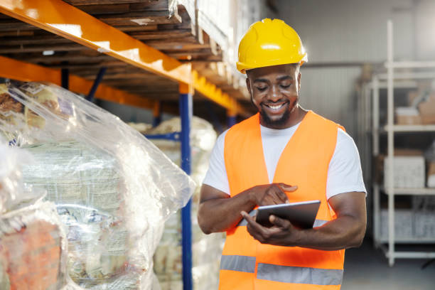 istock Smiling black blue collar worker standing at warehouse with tablet in hand and looking through checklist. 2181707080