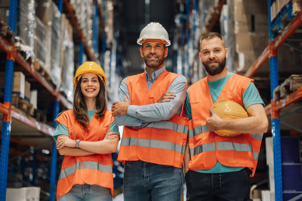 istock Warehouse workers posing with arms crossed wearing reflective vests and hard hats 2181712036