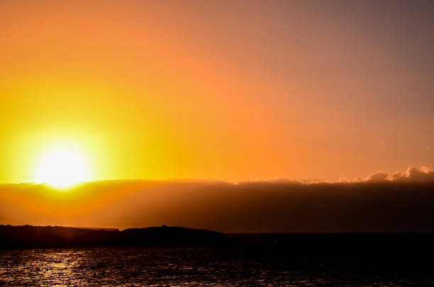The sun is setting over the ocean, casting a warm glow over the water. The sky is a mix of orange and pink hues, creating a serene and peaceful atmosphere