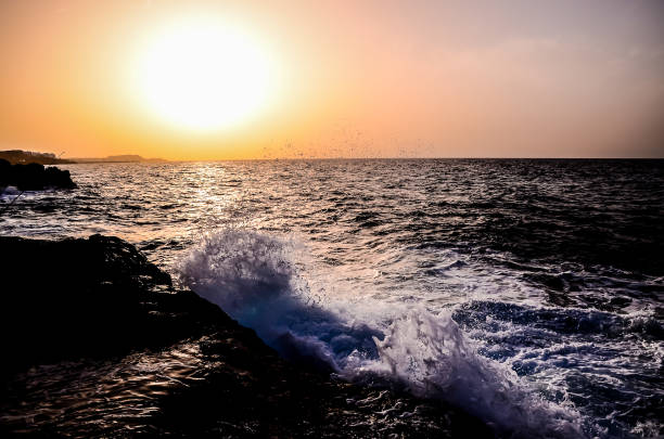 The ocean is calm and the sun is setting. The sky is a beautiful mix of orange and pink hues