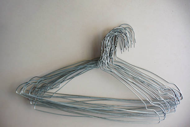 This close-up image focuses on the details of a clothing rack in a retail store. A row of light-colored wooden hangers hangs on a metal rail, with the primary focus on the white plastic size indicators attached to the chrome hooks. The central marker is sharply defined, displaying the letter \