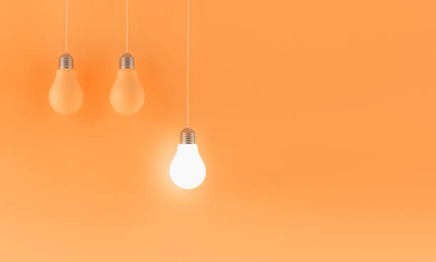 istock Three Hanging Lightbulbs on Orange Background, One Illuminated 2181722573