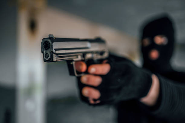 Criminal in black mask holding handgun, preparing to fire