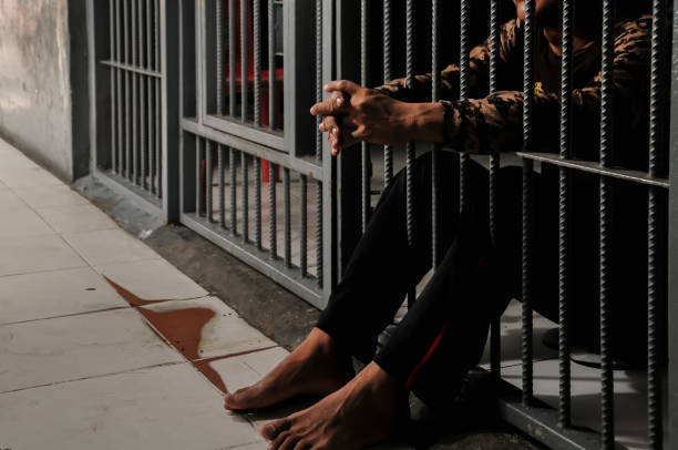 istock hands of a prisoner behind prison bars on black background 2181727173