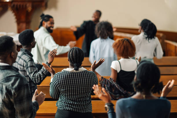 Group of people raising their hands while praying inside the church Diverse group of churchgoers are emotionally singing and raising their hands while praying together inside the church black gospel church stock pictures, royalty-free photos & images