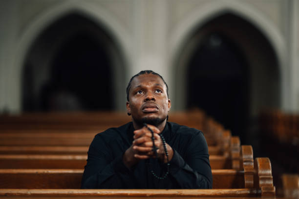 istock Young priest praying with rosary beads in church 2181729159