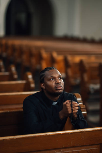 istock Priest praying with rosary beads in church pew 2181729191