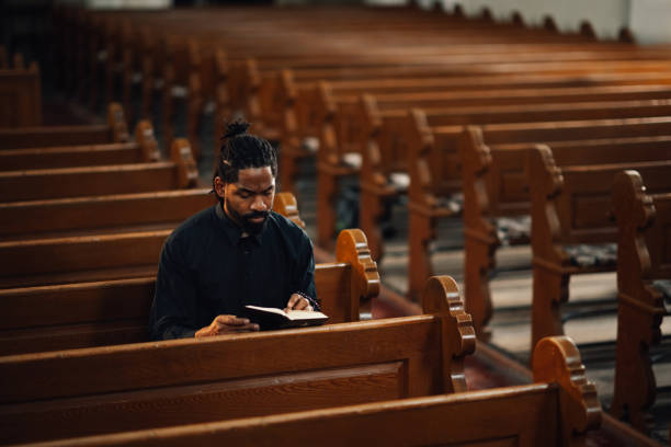 istock Priest reading holy bible sitting on bench in church 2181729196
