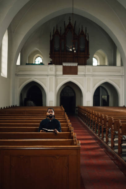 istock Priest sitting in church pew reading bible 2181729197