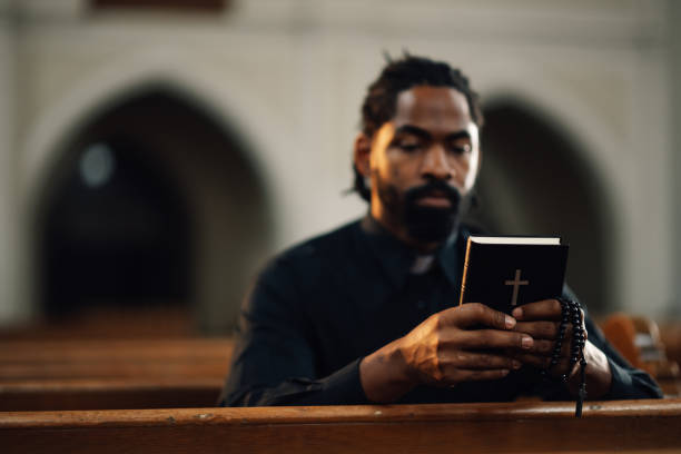 istock Priest reading holy bible sitting on bench in church 2181729199