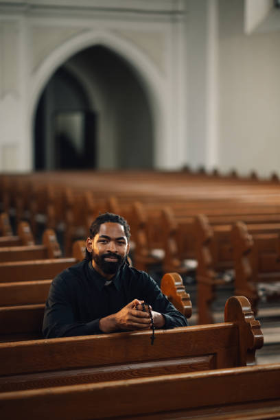 istock Priest praying with rosary beads sitting on bench in church 2181729220