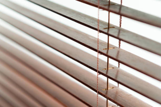 Close-up of wooden blinds with horizontal slats, showcasing the texture and details of the wood. Light filters through the gaps, creating a soft, diffused illumination.