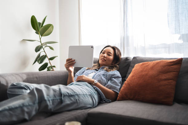 Relaxed woman using tablet on sofa at home in sunlight