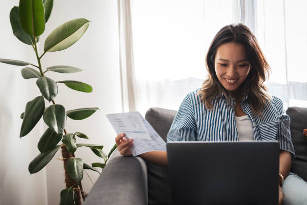 istock Asian woman reviewing documents on laptop at home 2181733009