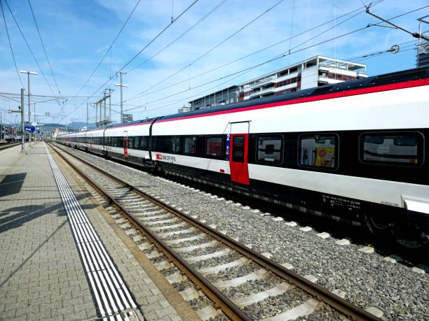 Frontal vertical view of a modern red locomotive cabin arriving into railway station depot; contemporary electric high-speed suburban train leaving the platform with tracks junction in front