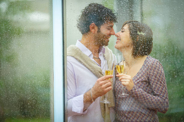istock Romantic couple sharing a toast behind rainy window on wedding day 2181741862