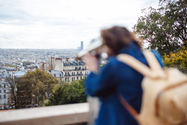 A tourist with a backpack uses binoculars to admire the panoramic view of Paris. The cityscape features historic architecture and a modern skyline, capturing the essence of both tradition and modernity.