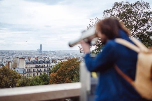 A tourist uses a public telescope to admire the panoramic view of Paris, capturing the essence of exploration and discovery. The cityscape includes iconic architecture and autumn trees, adding to the enchanting atmosphere.