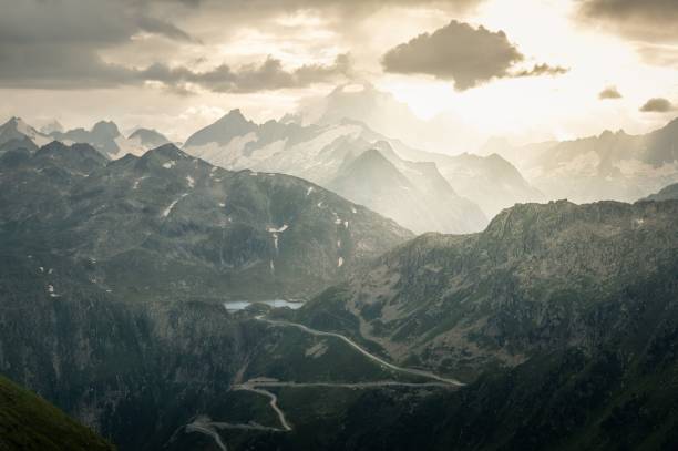 A Dramatic sunset over the Swiss Alps with clouds casting soft, muted tones on rugged peaks