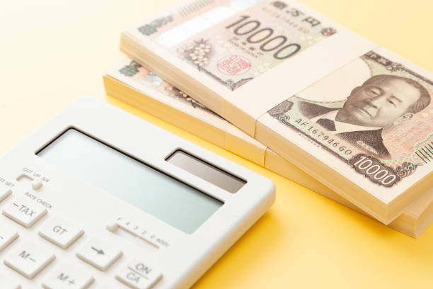 a stack of 10,000 yen bills and a calculator on a yellow background. - 給付金 ストックフォトと画像