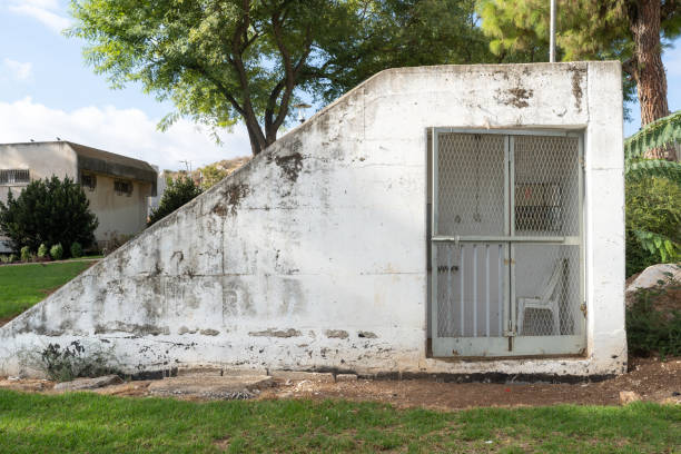 An outdoor bomb shelter in Israel, surrounded by green grass and trees, showing the rugged texture of its concrete walls. The structure stands as a reminder of security and resilience.