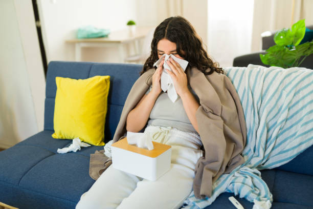 istock Sick teen girl with cold and flu symptoms blowing her nose with tissues while resting on sofa at home 2181757574