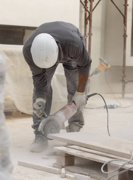 istock Craftsman in grey work clothes and helmet cutting marble piece during construction 2181758913