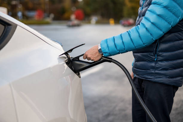istock Man inserts a power cord into an electric car for charging 2181759633