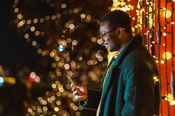 istock Young African American man enjoying festive lights while browsing his smartphone 2181760789