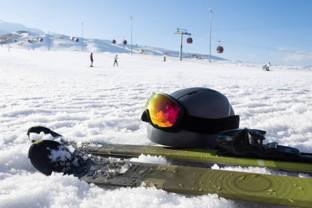 Mountain skis, ski sticks, ski helmet with sunscreen mask on bright alpine snow on background of ski slope with ski lifts and a cloundy sky. Winter holidays. Extreme sport. Vacation, travel content. Copy space