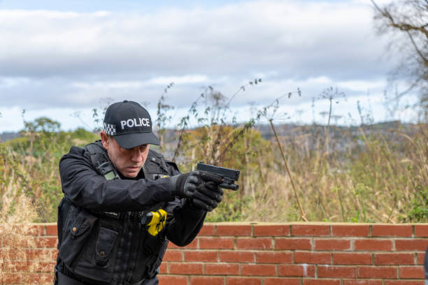 Armed UK police officer wearing baseball cap.  He is aiming at a driver in a car.