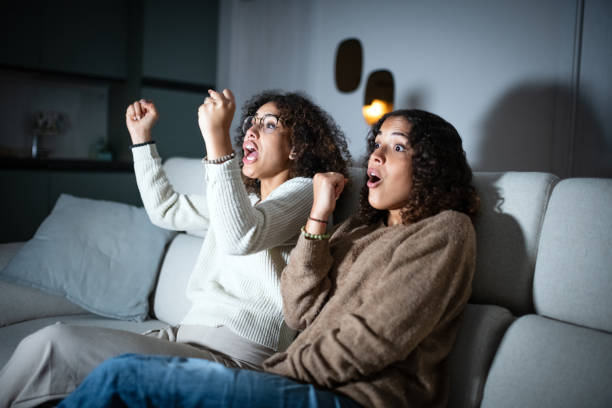 istock Sisters watching TV on sofa: Celebrating 2181768330