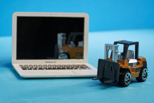 miniature laptop and forklift model  on blue background. Courier service