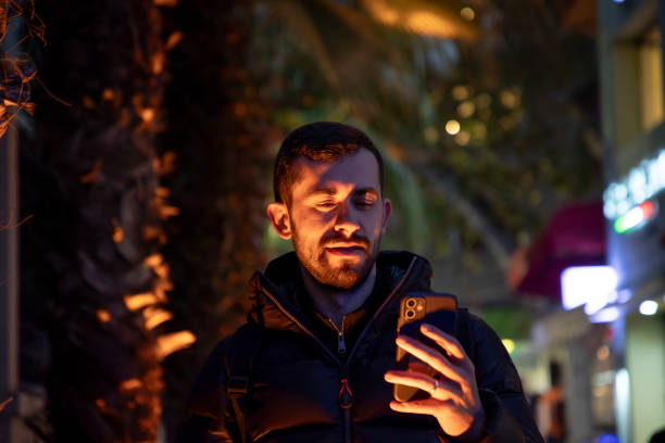 istock Young man texting on his phone under street lights 2181773913