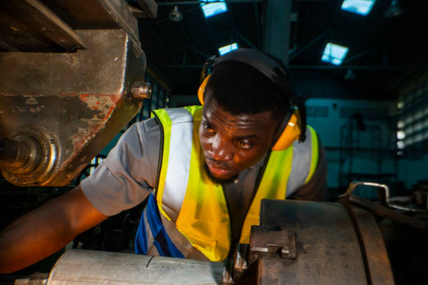 istock Industrial worker focused intently on operating a large gear-driven machine in a workshop. Safety gear such as ear protection and a reflective vest highlight the importance of safety in industrial. 2181774055