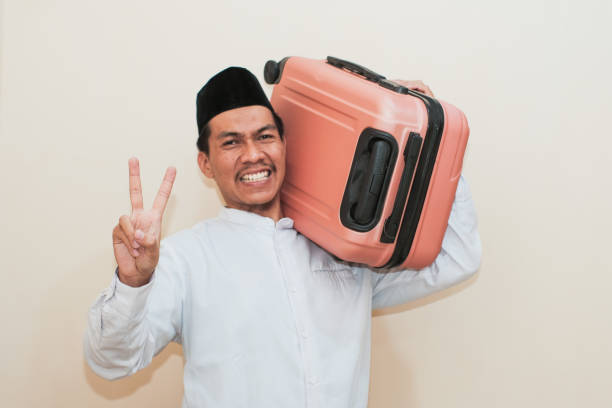 istock Excited Southeast Asian Muslim man carrying suitcase while showing two finger, Isolated on white background. 2181776237