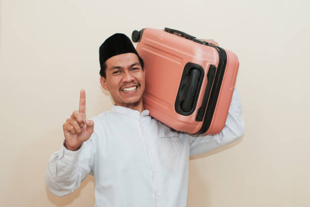 istock Excited Southeast Asian Muslim man carrying suitcase while showing one finger, Isolated on white background. 2181776250