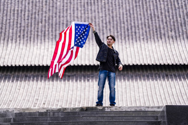 istock Young man proudly holds an American flag while standing on steps, symbolizing patriotism and pride. The flag's vibrant colors contrast with the subdued background, emphasizing national pride. 2181776556