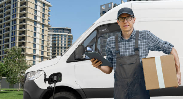istock Delivery man in uniform with digital tablet next to electric van. 2181778577
