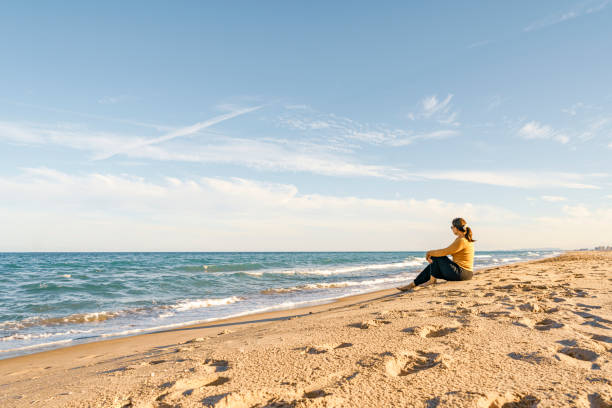 Woman sitting on the beach sand looking at horizon