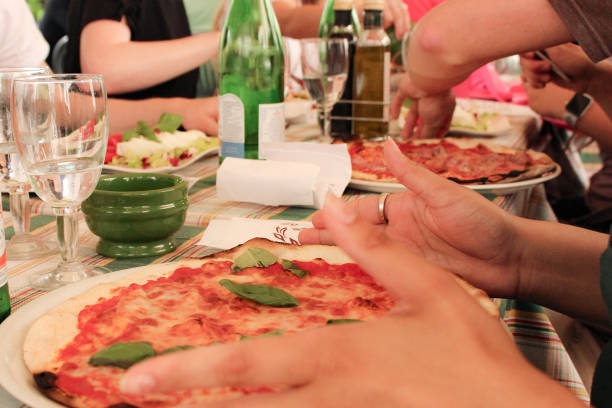 A group of friends eating pizza and drinking sparkling water at a cafe in Rome. Hands and torsos are visible but no distinguishable characteristics.