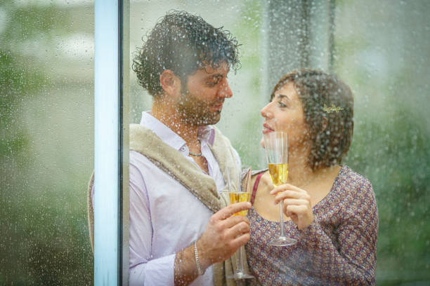 istock Romantic couple sharing a toast behind rainy window on wedding day 2181789383