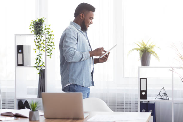 istock Black businessman using digital tablet, standing near window in office 2181789568