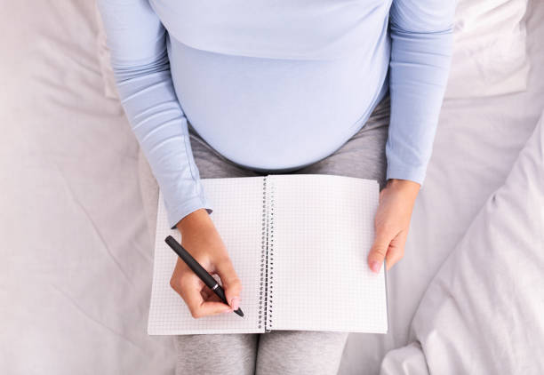 istock Unrecognizable Pregnant Woman Taking Notes Sitting On Bed Indoor, Top-View 2181795832