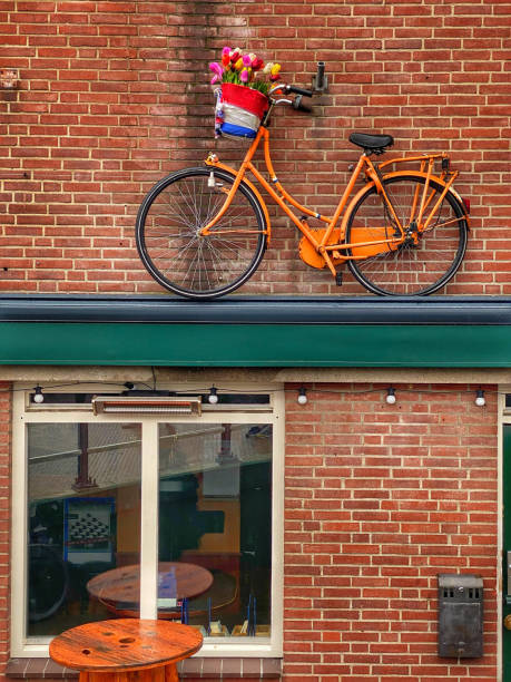 Orange bicycle with flower basket hanging on a brick wall in Delft, Netherlands.