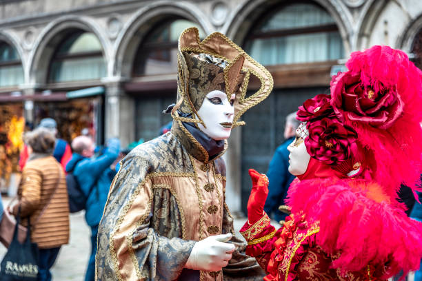 Venice, Italy - February, 23. 2014: Two people wearing carnival costume and mask posing for casual photographers under Ducal Palace colonnade in St. Mark square