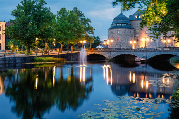 Orebro, Sweden- August 4, 2024: Illuminated Orebro Castle and stone bridge in blue hour . Tourist atraction and history entusiast destination.