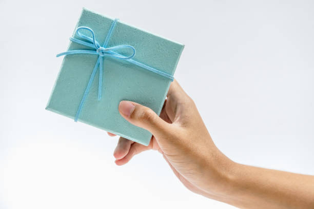 istock A hand holding a small, beautifully wrapped gift box with a blue ribbon, symbolizing celebration and surprise. 2181812657